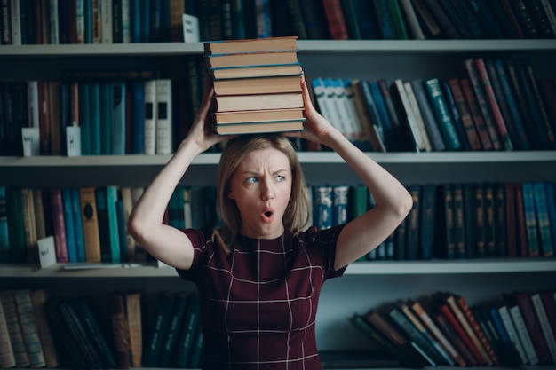 Menina loura bonita nova da mulher do estudante com livros da pilha