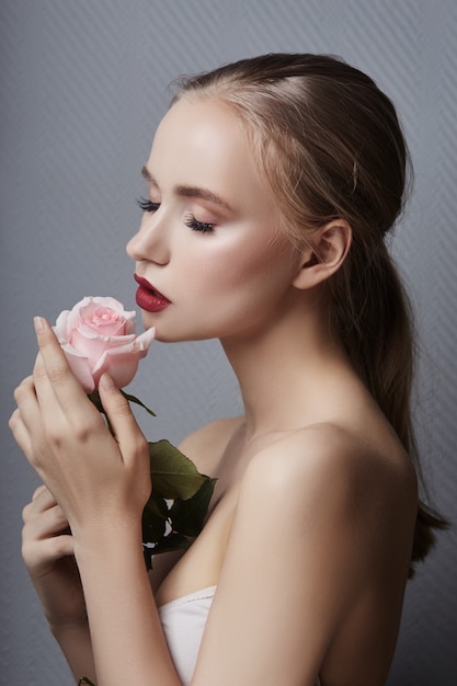 Menina loura que guarda flores cor-de-rosa perto da cara. Beleza