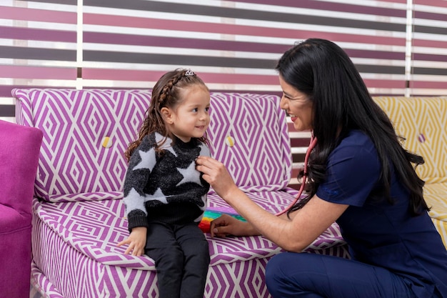 Menina macia olha para o médico enquanto é examinada com um estetoscópio no consultório médico