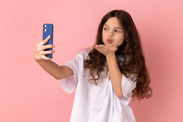 Menina mandando beijo no ar na câmera do smartphone enquanto se comunica por videochamada streaming vlog