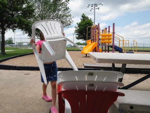 Foto menina mantendo a cadeira junto à mesa de piquenique no parque