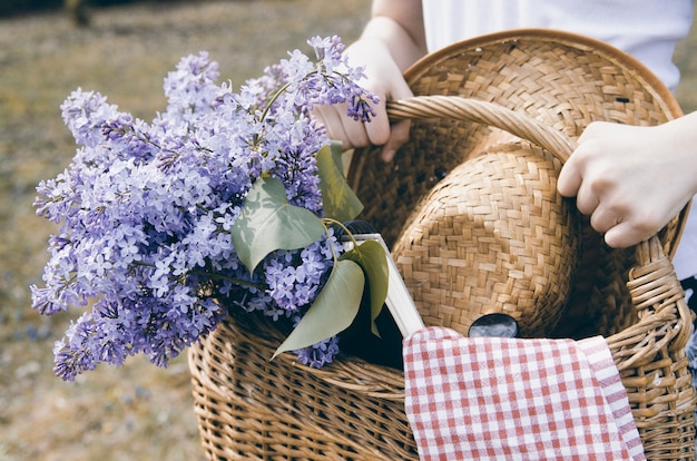 Menina mãos carregando cesta de vime com buquê de flores lilás