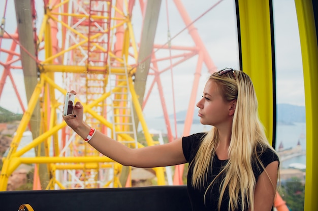 Foto menina moda jovem tirar selfie na roda gigante.