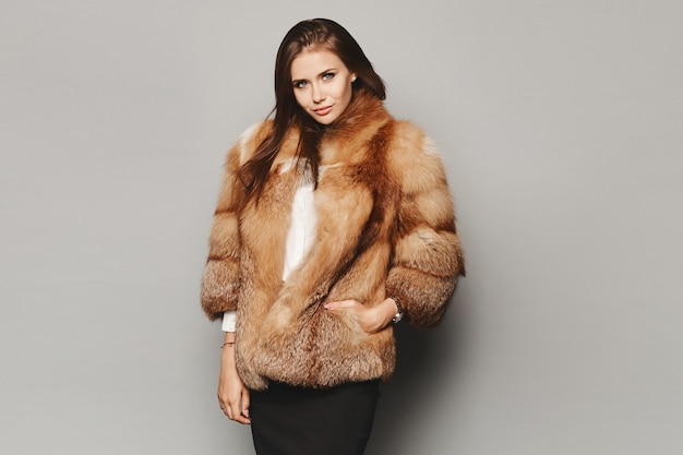 Menina modelo com um luxuoso casaco de pele de inverno no fundo cinza, isolado. Moda de inverno.