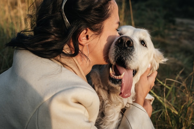 menina morena abraçando golden retriever branco no campo