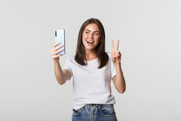 Menina morena atraente parecendo feliz e tirando uma selfie no smartphone
