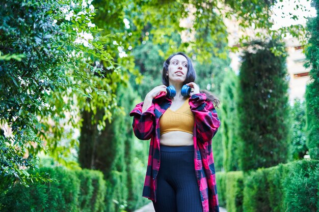 Menina morena caminhando pelos jardins do parque ouvindo música com fones de ouvido