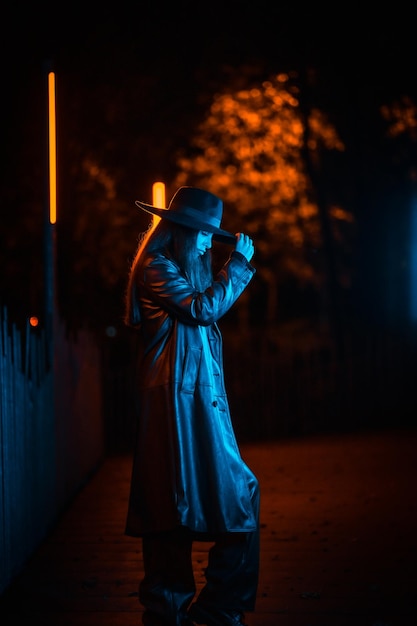 Menina morena caucasiana com chapéu à noite em um parque iluminado com luz azul