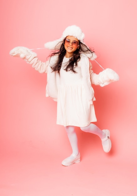 Menina morena com cabelo comprido, em um chapéu de pele de inverno e luvas em um fundo rosa.