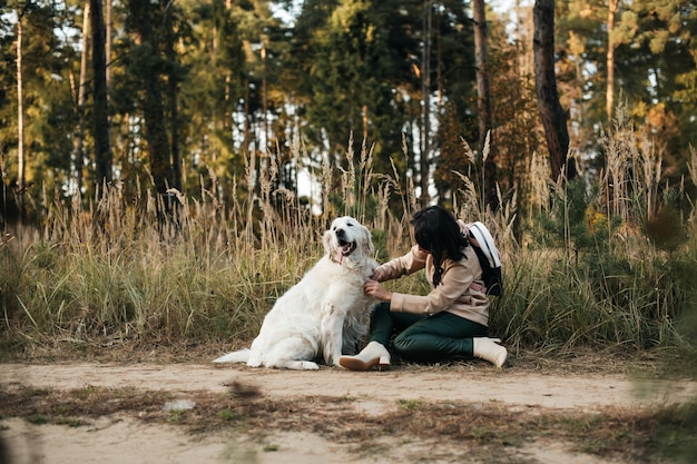 Menina morena com cachorro retriever dourado branco no caminho da floresta