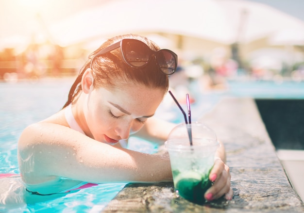 Menina morena com cocktails relaxantes na piscina. mulher de biquíni, aproveitando o sol de verão e bronzeamento durante as férias na piscina com bebida.