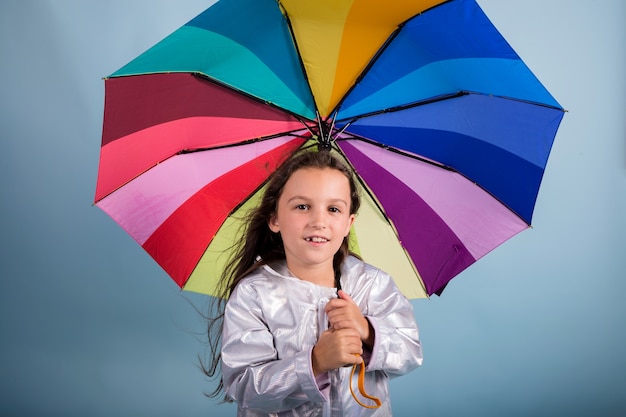Menina morena com um guarda-chuva multicolorido sobre um fundo azul com uma cópia do espaço