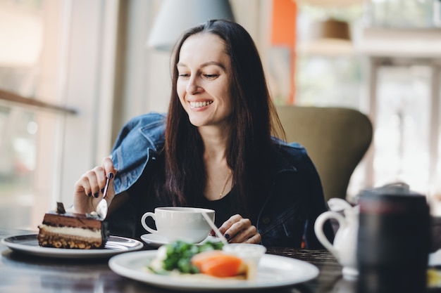 Foto menina morena comendo bolo no restaurante. aproveitando a comida