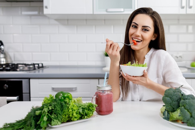 Menina morena comendo salada e bebendo smoothie