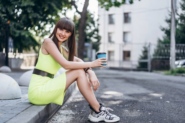 Menina morena de cabelo comprido, vestido verde com copo de papel azul