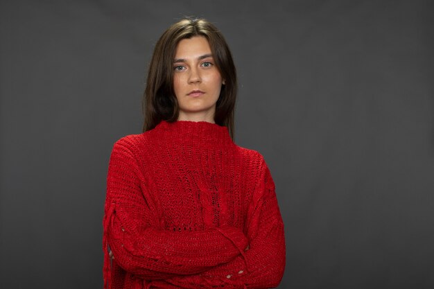 Menina morena de cabelos compridos, muito calma, posando com os braços cruzados em um suéter vermelho