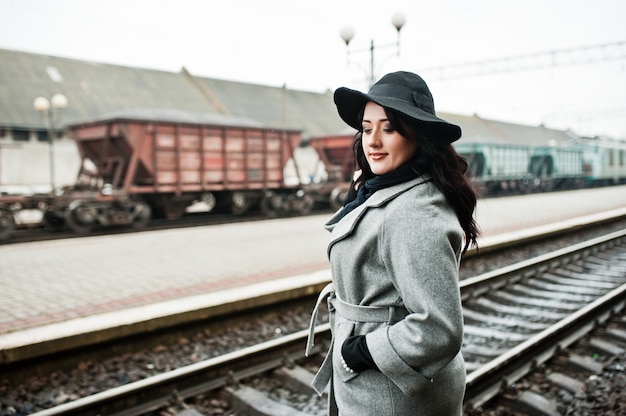 Menina morena de casaco cinza com chapéu na estação ferroviária