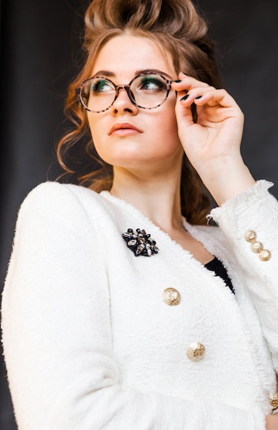 Menina morena elegante posando em um fundo preto em uma elegante jaqueta branca e óculos