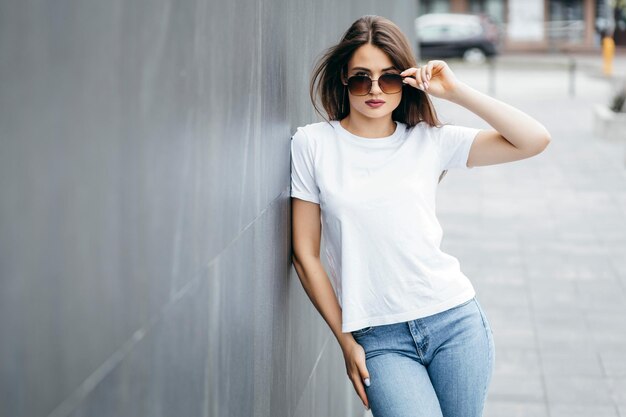 Menina morena elegante usando camiseta branca e óculos posando contra o estilo de roupa urbana de rua