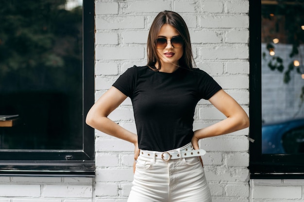 Foto menina morena elegante usando camiseta preta e óculos posando contra o estilo de roupa urbana de rua