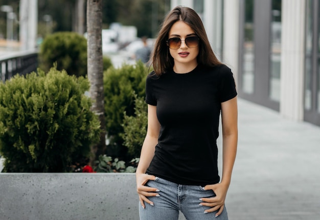 Menina morena elegante usando camiseta preta e óculos posando contra o estilo de roupa urbana de rua