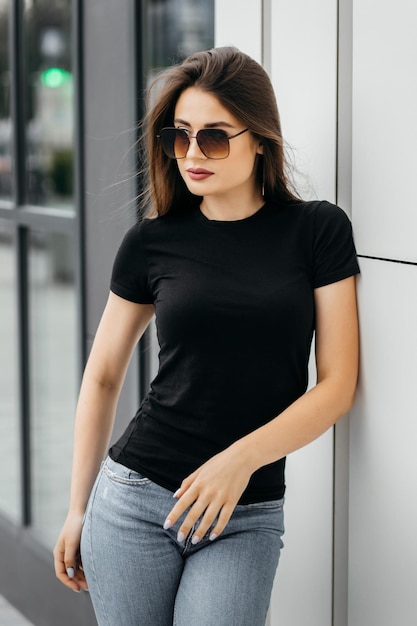 Foto menina morena elegante usando camiseta preta e óculos posando contra o estilo de roupa urbana de rua