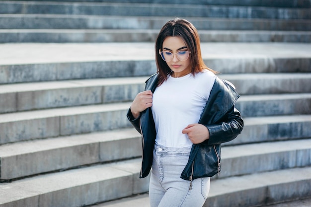 Menina morena elegante vestindo camiseta branca e óculos posando contra o estilo de roupas urbanas de rua