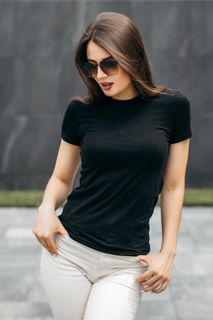 Menina morena elegante vestindo camiseta preta e óculos posando contra o estilo de roupas urbanas de rua