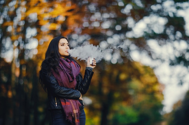 menina morena está fumando um cigarro no parque drung outono