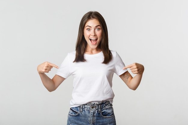 Menina morena feliz animada sorrindo, apontando o dedo para o logotipo, mostrando o banner.