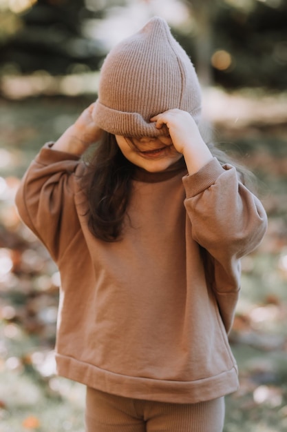 menina morena feliz com um chapéu de malha caminha no parque no outono