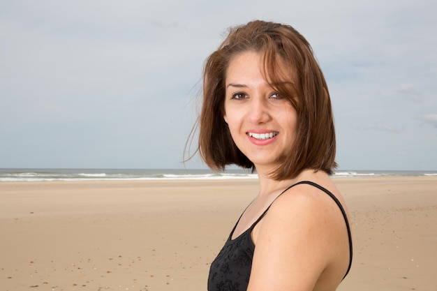 Menina morena feliz de vestido preto posando na praia