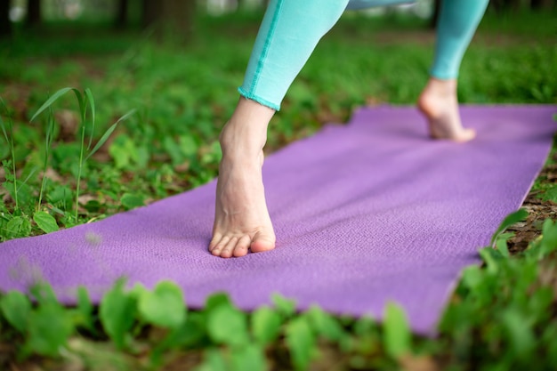 Menina morena fina pratica esportes e executa poses de ioga em um parque de verão. Mulher fazendo exercícios no tapete de ioga, close-up de pés
