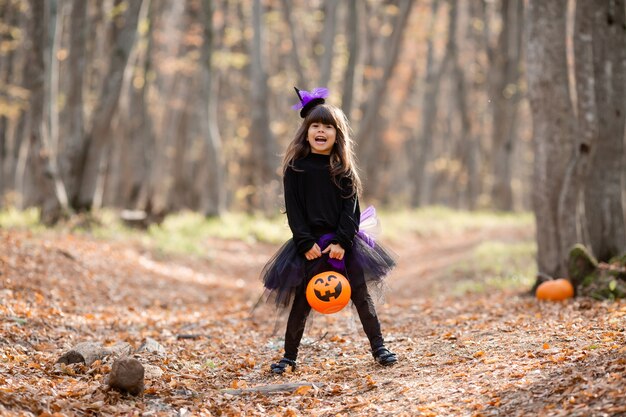 menina morena fofa com fantasia de bruxa de Halloween com uma cesta de abóbora nas mãos