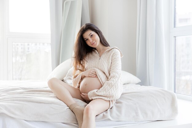 Menina morena grávida em um suéter de malha de grandes dimensões