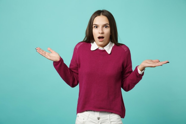 Menina morena jovem em roupas casuais posando espalhando as mãos isoladas no retrato de estúdio de fundo de parede azul verde turquesa. Conceito de estilo de vida de pessoas. Mock up espaço de cópia. Olhando o sorriso da câmera