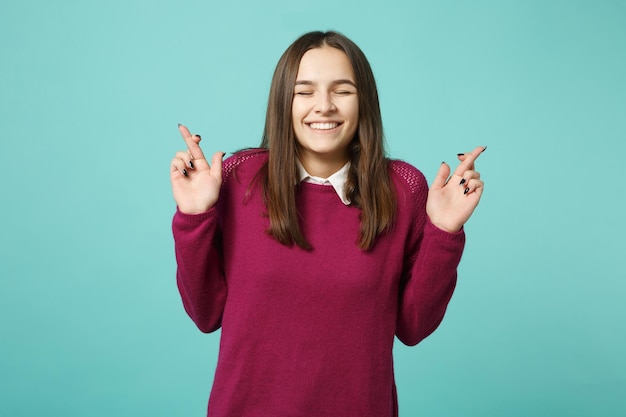 Menina morena jovem em roupas casuais posando isolado no retrato de estúdio de fundo azul verde turquesa. Conceito de estilo de vida de emoções sinceras de pessoas. Mock up espaço de cópia. mantendo os dedos cruzados.