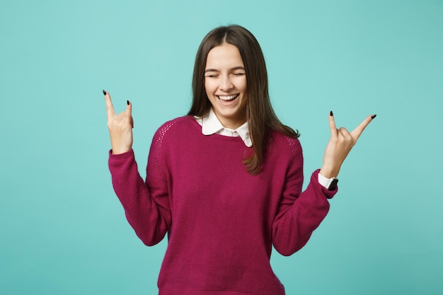 Menina morena jovem em roupas casuais posando isolado no retrato de estúdio de fundo de parede azul verde turquesa. Conceito de estilo de vida de emoções sinceras de pessoas. Mock up espaço de cópia. gesto de chifres para cima.