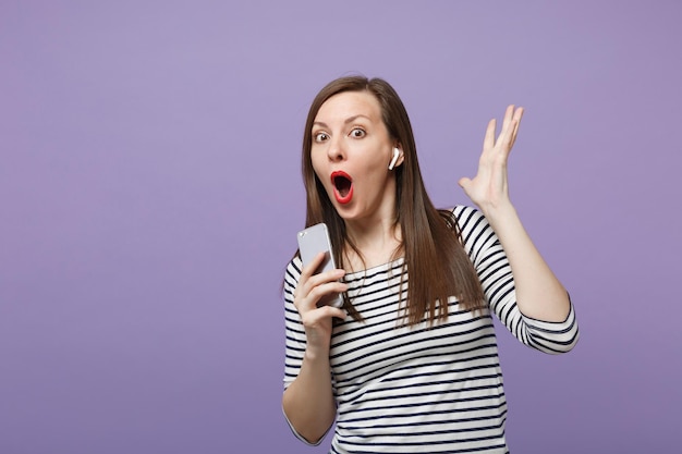 Menina morena jovem em roupas listradas casuais posando isolado no retrato de estúdio de fundo roxo violeta. Conceito de estilo de vida de emoções sinceras de pessoas. Mock up espaço de cópia. Segure a conversa do telefone móvel.