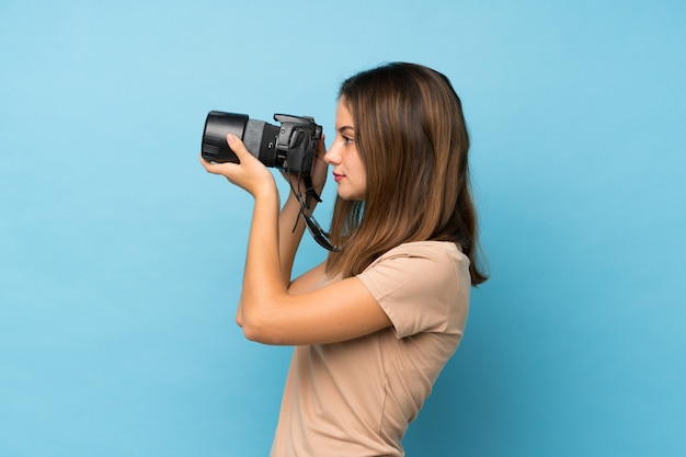 Menina morena jovem isolado azul com uma câmera profissional