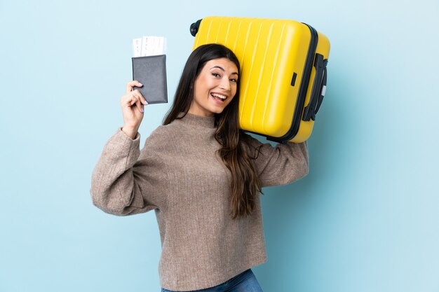 Menina morena jovem isolado parede azul em férias com mala e passaporte