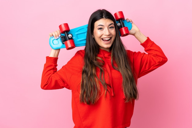 Menina morena jovem isolado rosa com um skate