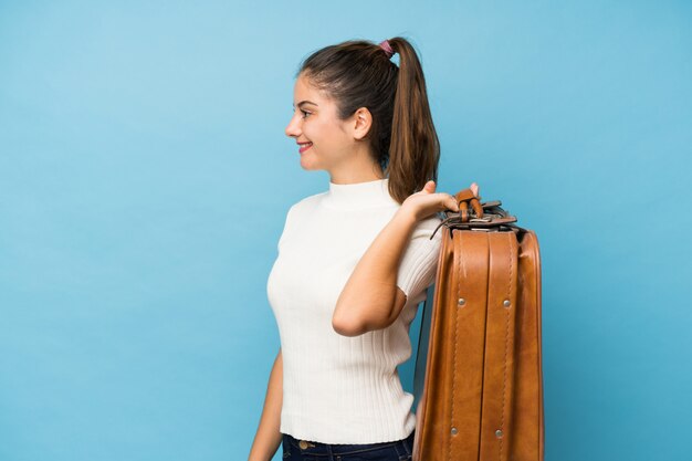 Menina morena jovem sobre azul isolado, segurando uma mala vintage