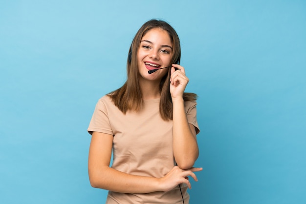 Menina morena jovem sobre parede azul isolada, trabalhando com fone de ouvido