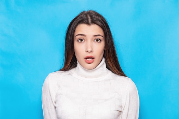 Menina morena jovem surpresa, chocada em roupas brancas casuais, posando isolado no retrato de estúdio de fundo de parede azul pastel. Conceito de estilo de vida de pessoas. Simule o espaço da cópia. Mantendo a boca aberta