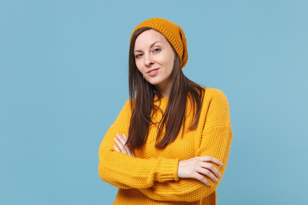 Menina morena linda camisola amarela e chapéu posando isolado no retrato de estúdio de fundo azul. Conceito de estilo de vida de emoções sinceras de pessoas. Mock up espaço de cópia. De mãos dadas cruzadas.