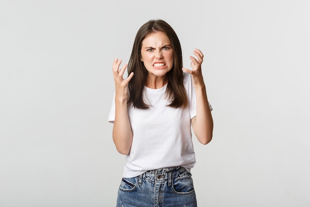 Menina morena louca e furiosa, apertando as mãos e fazendo uma careta de raiva.