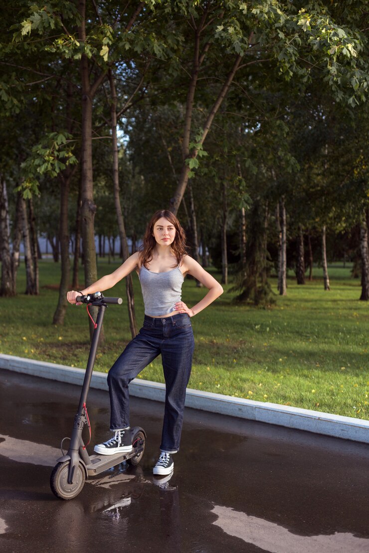 Menina morena, montando uma scooter elétrica ecofriendly em um parque em tempo ensolarado nas calçadas