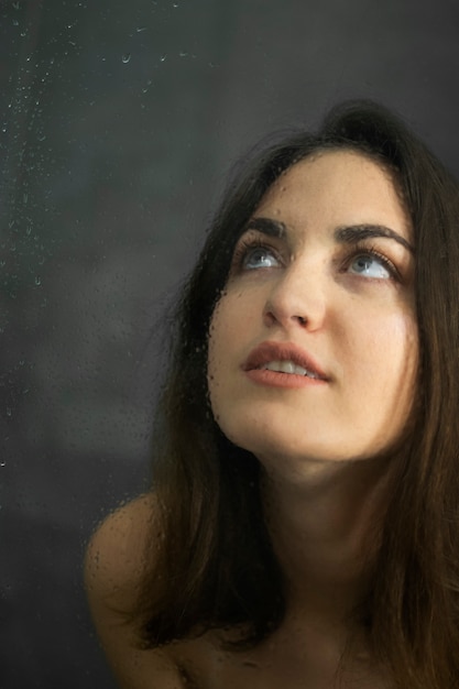 Foto menina morena no chuveiro. gotas de água na tela do chuveiro. retrato