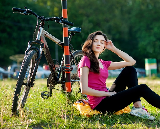 Menina morena no sportswear rosa com uma bicicleta a descansar e relaxar